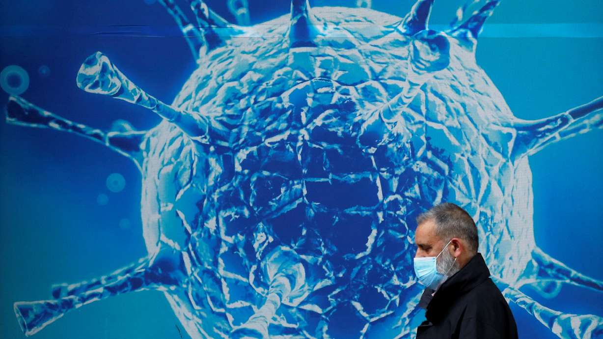 FILE PHOTO: A man wearing a protective face mask walks past an illustration of a virus outside a regional science centre, as the city and surrounding areas face local restrictions in an effort to avoid a local lockdown being forced upon the region, amid the coronavirus disease (COVID-19) outbreak, in Oldham, Britain Aug. 3, 2020.
