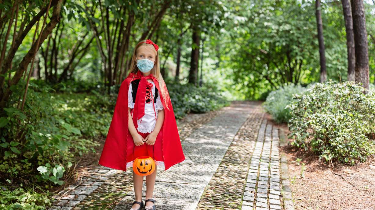Portrait of cute Little Girl in costume of red hat in the park. Happy Halloween during coronavirus covid-19 pandemic quarantine concept. Kid wearing medical mask