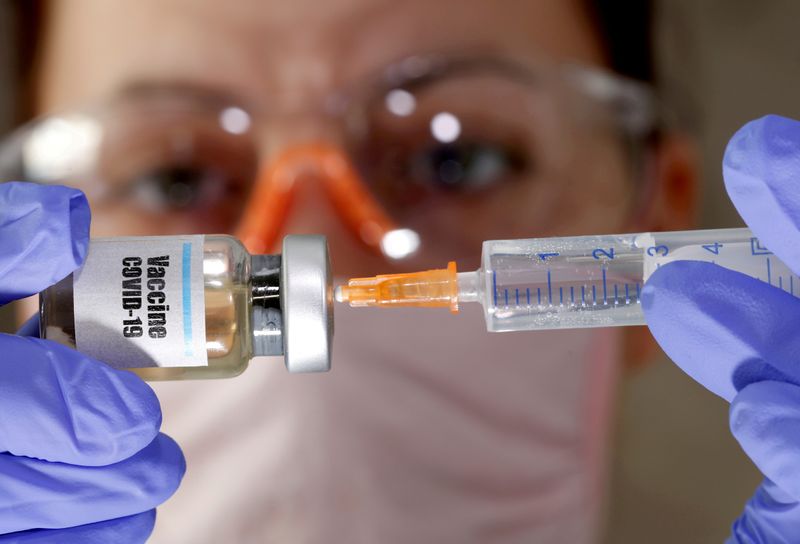 FILE PHOTO: A woman holds a small bottle labeled with a "Vaccine COVID-19" sticker and a medical syringe in this illustration taken April 10, 2020. REUTERS/Dado Ruvic/File Photo