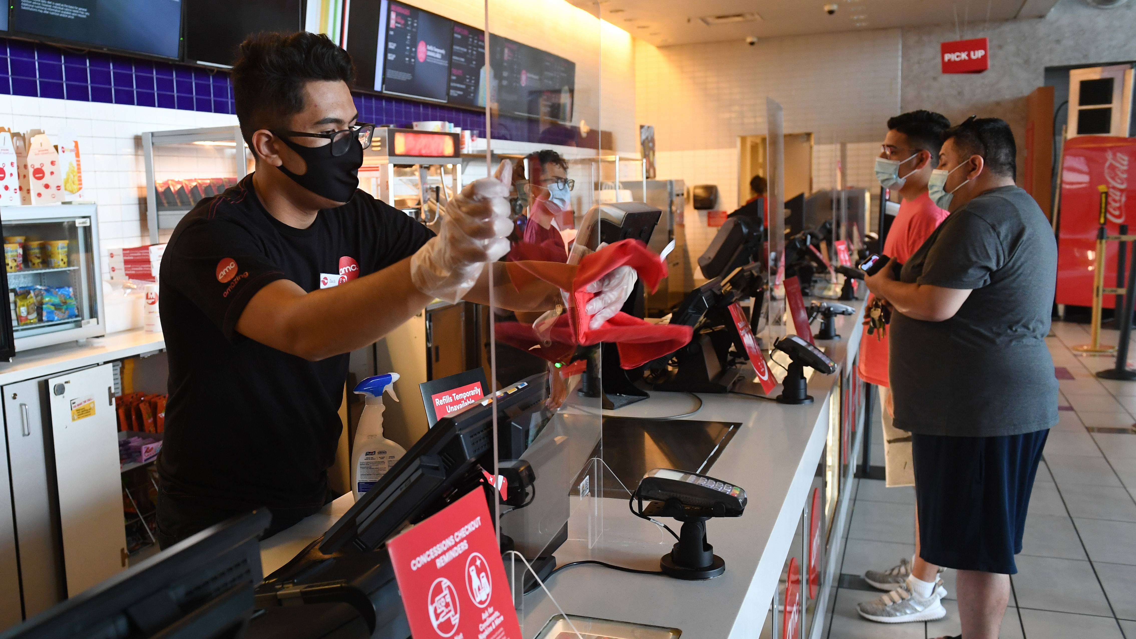 LAS VEGAS, NEVADA - AUGUST 20:  Zach Fontana sanitizes a plexiglass safety shield divider at the concession stand at AMC Town Square 18 on Aug. 20, 2020 in Las Vegas, Nevada. AMC Theatres reopened more than 100 of its movie theaters across the United States today, with new safety precautions in place, for the first time since closing in March because of the coronavirus (COVID-19) pandemic. In celebration of its 100th anniversary, the world's largest theater chain is welcoming guests back with a "Movies in 2020 at 1920 Prices" promotion for one day by offering 15-cent tickets to classic and previously-released films and USD 5 concession items. Starting on August 21, older movies will be shown for USD 5 a ticket. According to AMC, enhanced cleaning and safety protocols include disinfecting theaters before each show, mandatory face coverings for employees and customers, upgraded air filtration systems where possible, and high-touch points cleaned throughout the day. Hand sanitizer and disinfectant wipes are available throughout the theaters, auditoriums are at 40 percent capacity or less, and concession menus have been simplified for shorter lines and quicker service.  (Photo by Ethan Miller/Getty Images)