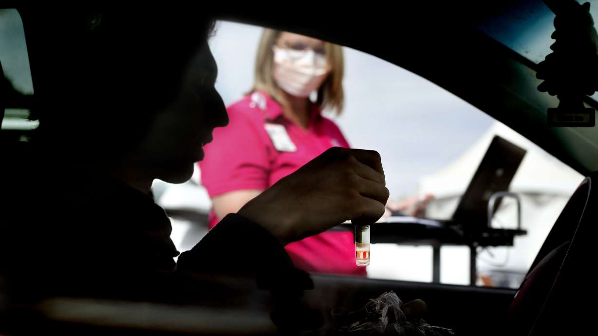 Sven Karabegovic holds his COVID-19 saliva test while giving his information to Tiffany Larsen at a drive-thru test site at University of Utah Health's South Jordan Health Center in South Jordan on Friday, Oct. 2, 2020.