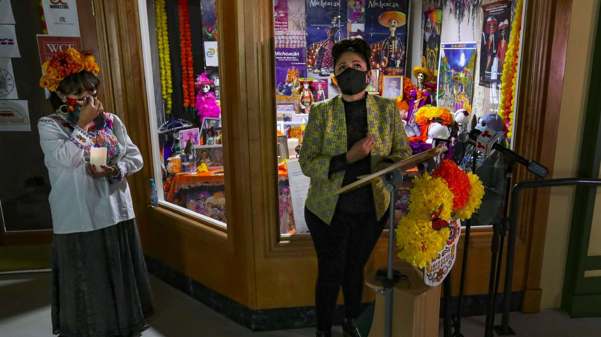 Artist Marla O. Lepe, center, holds back tears as she talks about her family and friends who have died and are represented in Una Mano Amig's Day of the Dead window display at Trolley Square in Salt Lake City on Wednesday, Oct. 28, 2020. This year, because of COVID-19, the organization designed the special social distancing window honoring family members, friends, first responders and others who died of the virus.
