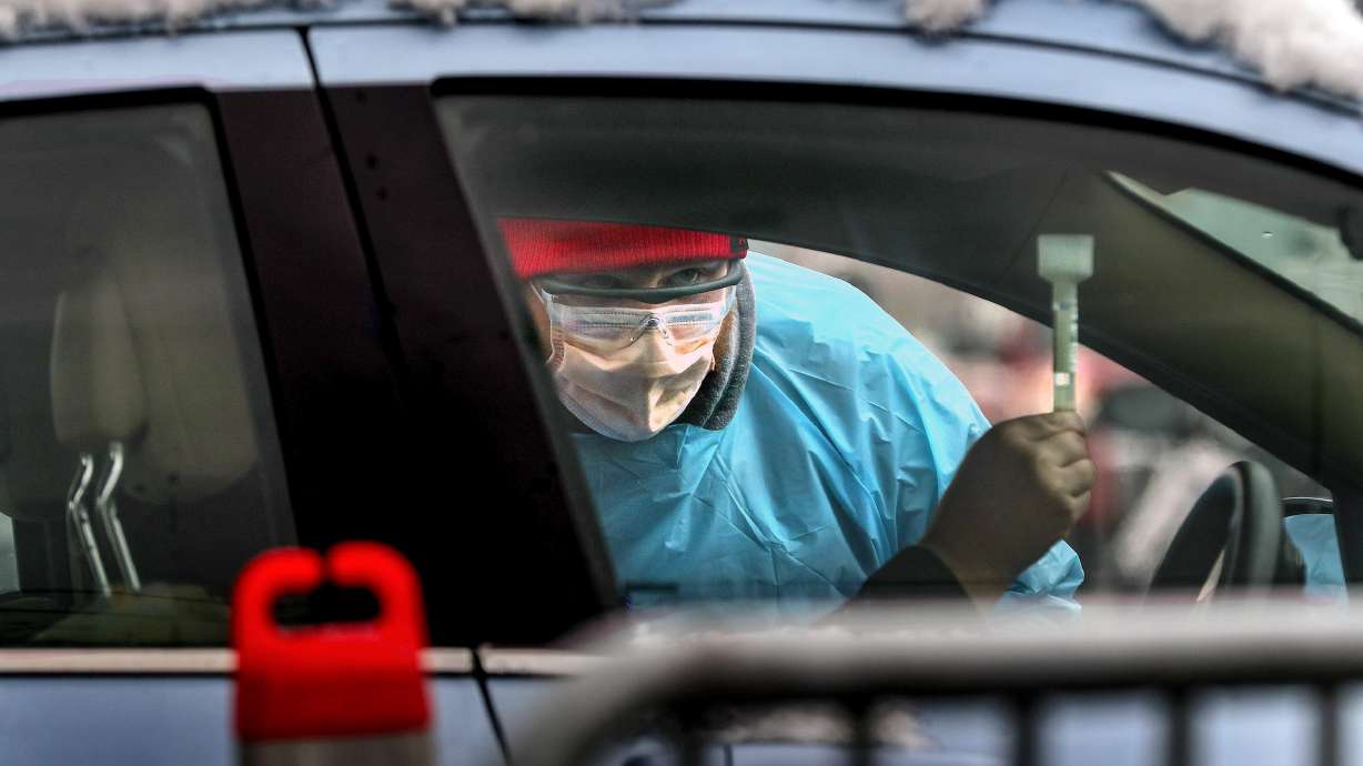 Spencer Moore, a medical assistant with University of Utah Health, checks a saliva sample as he administers a COVID-19 test at the Rice-Eccles Stadium testing site in Salt Lake City on Monday, Nov. 9, 2020.