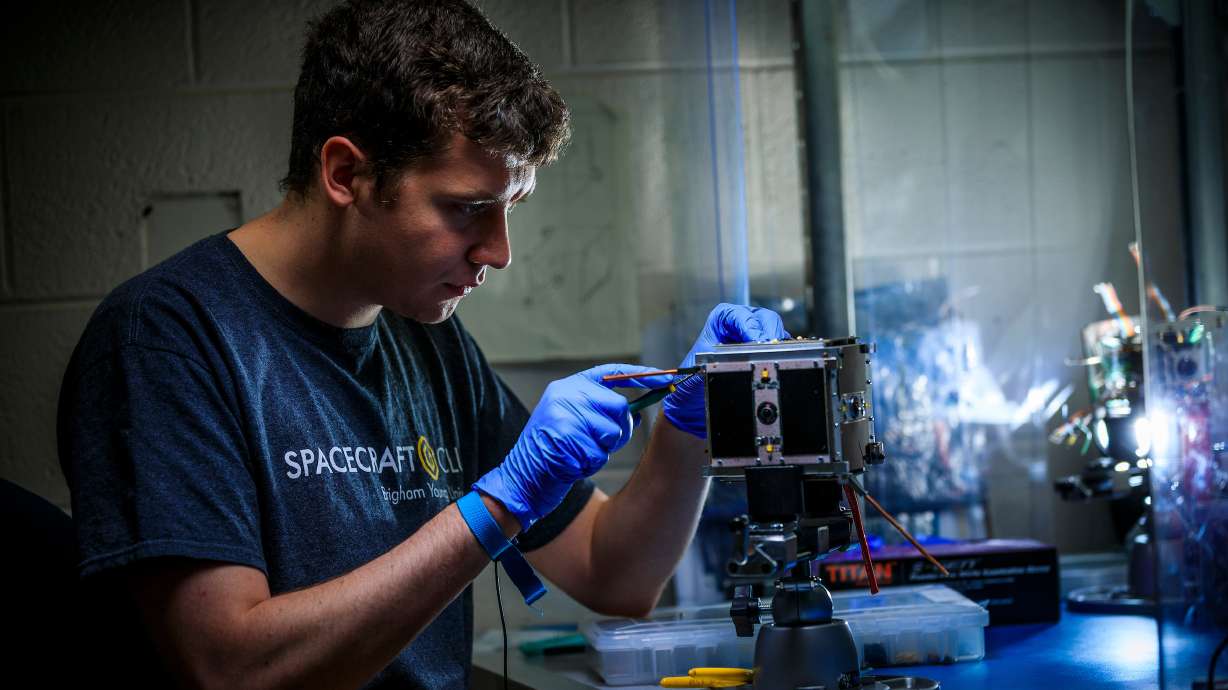 A student works on BYU's Cube Satellite in preparation for its official NASA launch.