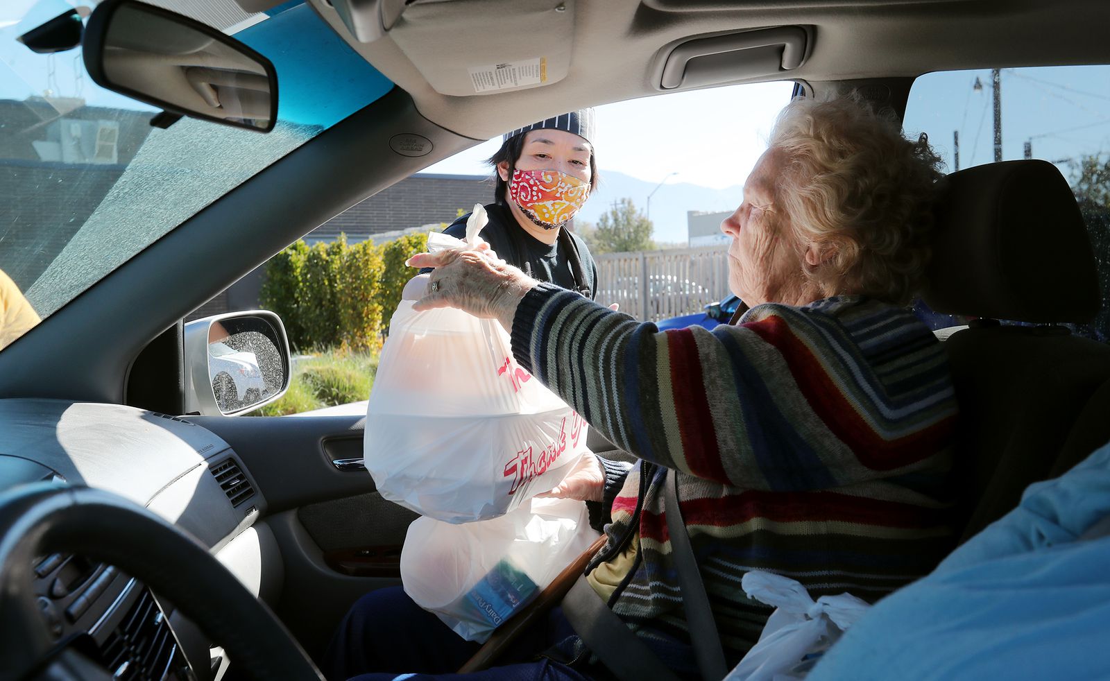 Food server Mari Orikasa hands Belva Frandsen bags of food as seniors drive up and receive lunches at the Midvale Senior Center on Monday, Nov. 2, 2020.