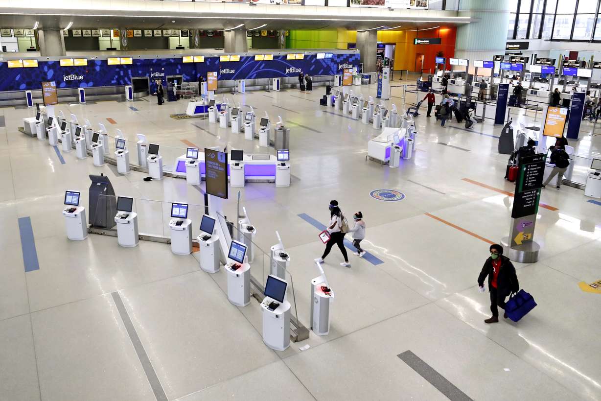 Travelers walk through the nearly empty JetBlue terminal at Logan Airport, Friday Nov. 20, 2020, in Boston. In Massachusetts, the state agency that operates Boston’s Logan Airport says it must cut about 25% of its workforce amid a $400 million budget deficit brought on by a steep drop in travel during the pandemic.