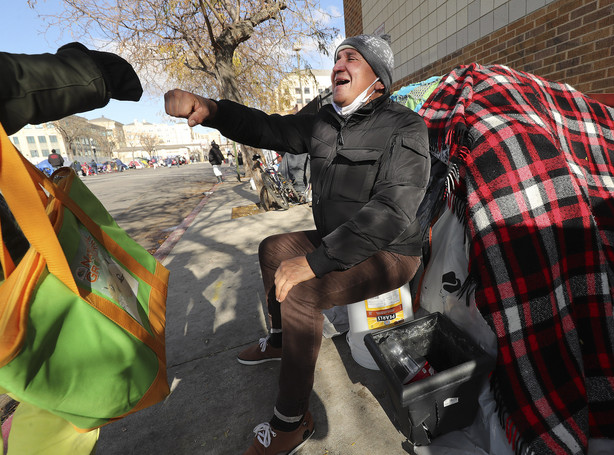 Jose Vasquez, who is homeless, greets a friend near his tent in Salt Lake City on Tuesday, Nov. 24, 2020. Volunteers with the Rescue Mission of Salt Lake volunteers delivered boxed meals to Vasquez and others during the organization's Two-Days-Before-Thanksgiving Banquet.