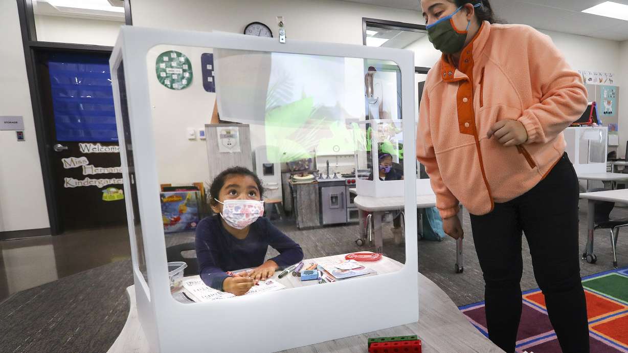Edison Elementary School kindergartener Rebeca Prado sits behind a protective screen as she works on English skills with her teacher Veronica Hernandez at the school in Salt Lake City on Monday, Nov. 23, 2020.
