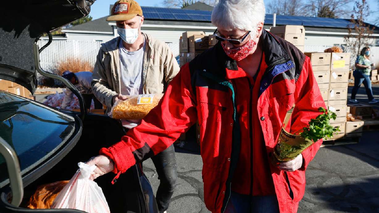 Austin Namba, left, and Tina Maxfield put food into a recipient's car during a food bank distribution event in the parking lot of a Church of Jesus Christ meetinghouse in West Jordan on Monday, Nov. 30, 2020.