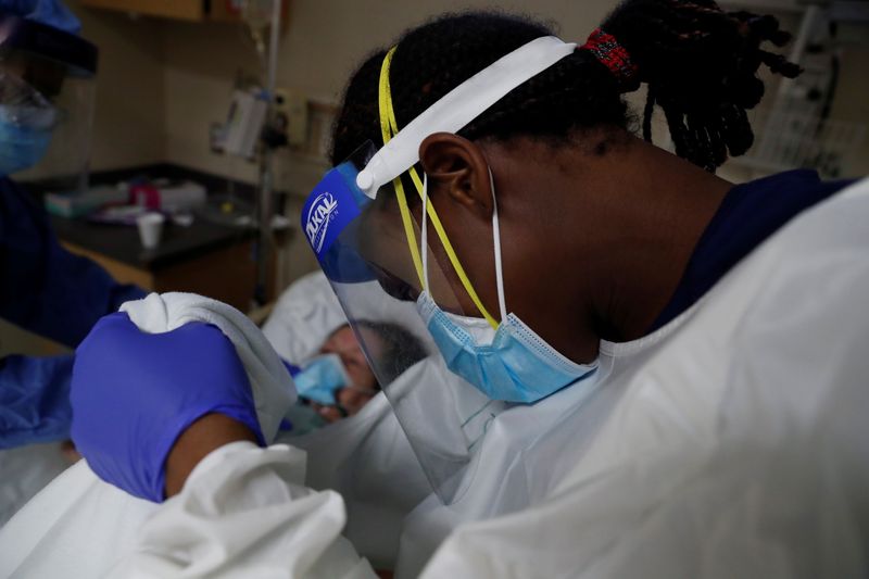 Patient Care Technician Fanta Keita treats Donna Plummer, a coronavirus disease (COVID-19) positive patient, as she lays on the emergency room bed at Roseland Community Hospital on the South Side of Chicago, Illinois, U.S., Dec. 2, 2020. REUTERS/Shannon Stapleton