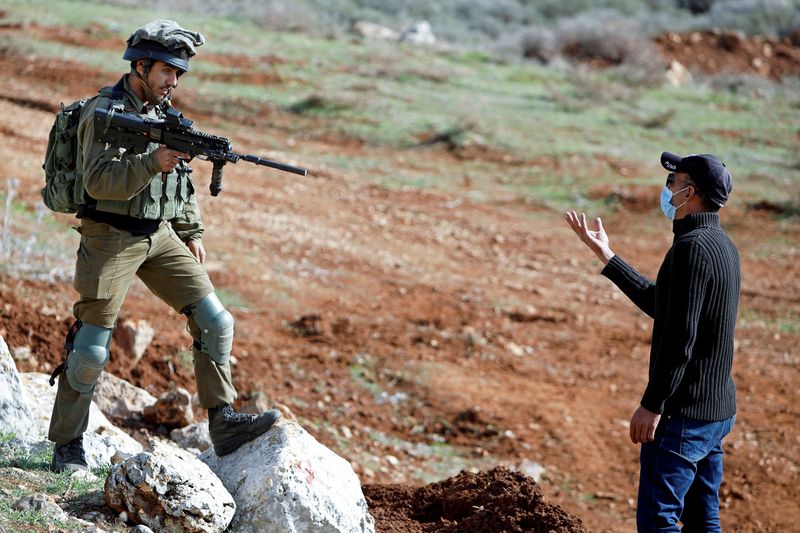 A Palestinian demonstrator stands in front of an Israeli soldier during a protest against Jewish settlements, in Beit Dajan in the Israeli-occupied West Bank December 4, 2020. REUTERS/Raneen Sawafta