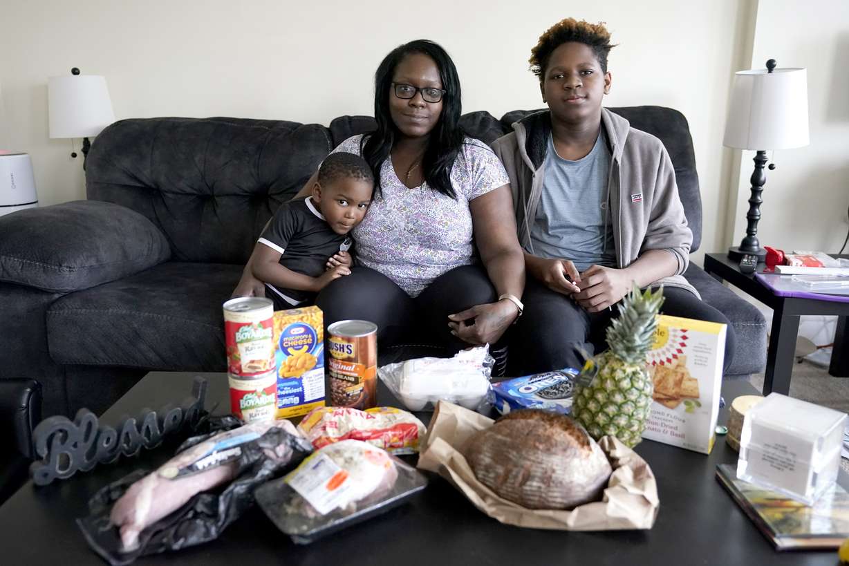 Briana Dominguez, center, sits with her sons, Noah Scott, 4, left, and Nehemiah Powell, 14, for a portrait inside their their Skokie, Ill., apartment with groceries she received at the Hillside Food Pantry. After her employer eliminated her job, the family is moving to Georgia where living costs are lower.