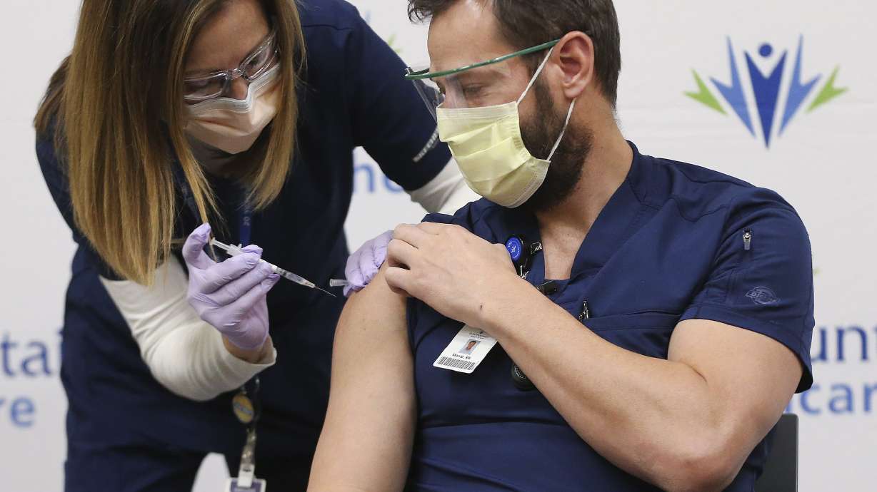 Registered nurse Julie Nelson, left, vaccinates fellow registered nurse Monte Roberts for COVID-19 at LDS Hospital in Salt Lake City on Tuesday, Dec. 15, 2020.