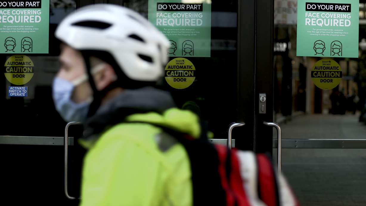 Joshua Mars walks past signs requesting people to do their part and wear a mask in Salt Lake City on Thursday, Nov. 12, 2020.