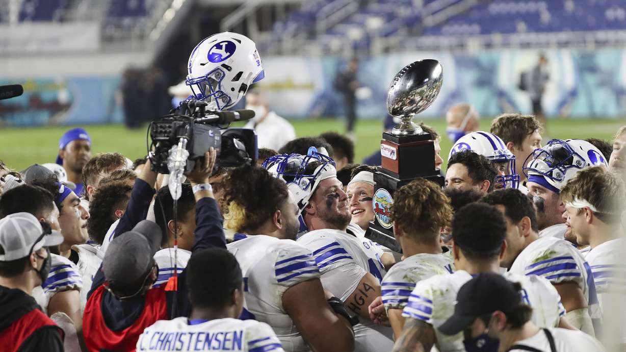 Brigham Young Cougars quarterback Zach Wilson (1), Brigham Young Cougars running back Lopini Katoa (4 )and Brigham Young Cougars offensive lineman Brady Christensen (67) hoist the trophy after the Boca Raton Bowl in Boca Raton, Fla., on Tuesday, Dec. 22, 2020. BYU won 49-23.