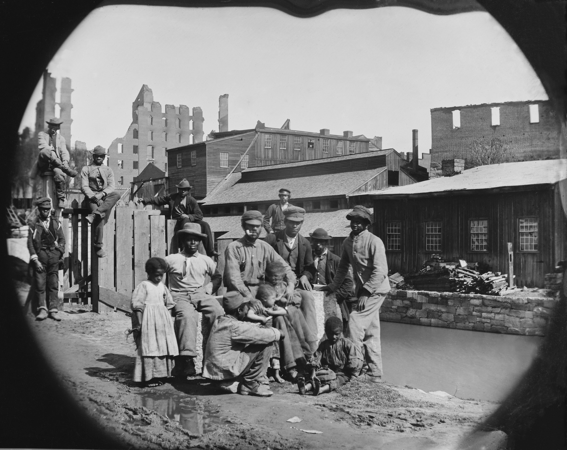 A newly freed African American group of men and a few children posing by a canal against the ruins of Richmond, Virginia. Photo made after Richmond was taken by Union troops on April 3, 1865.