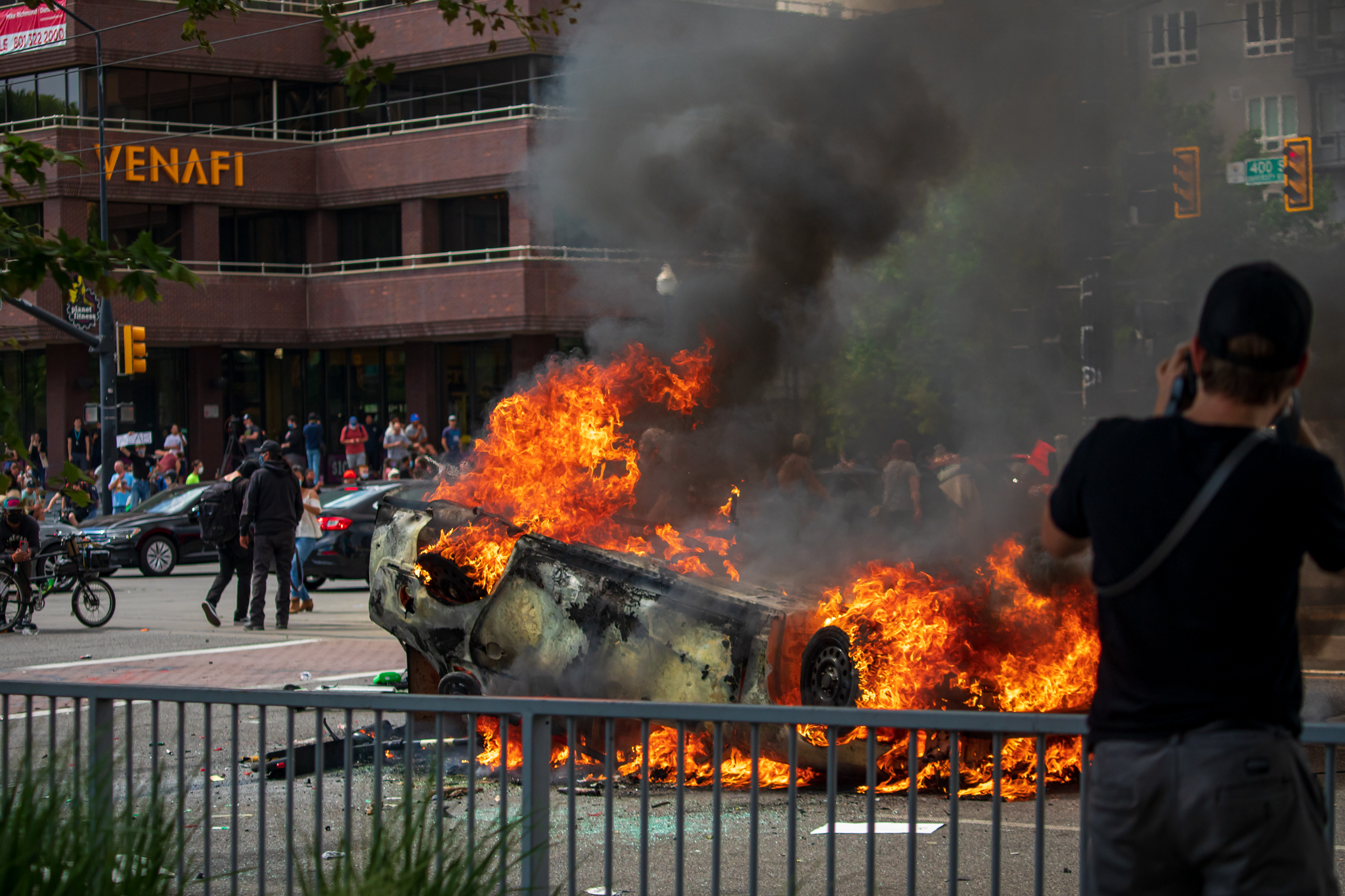 A man takes a photo of a burning police car in downtown Salt Lake City on May 30, 2020.