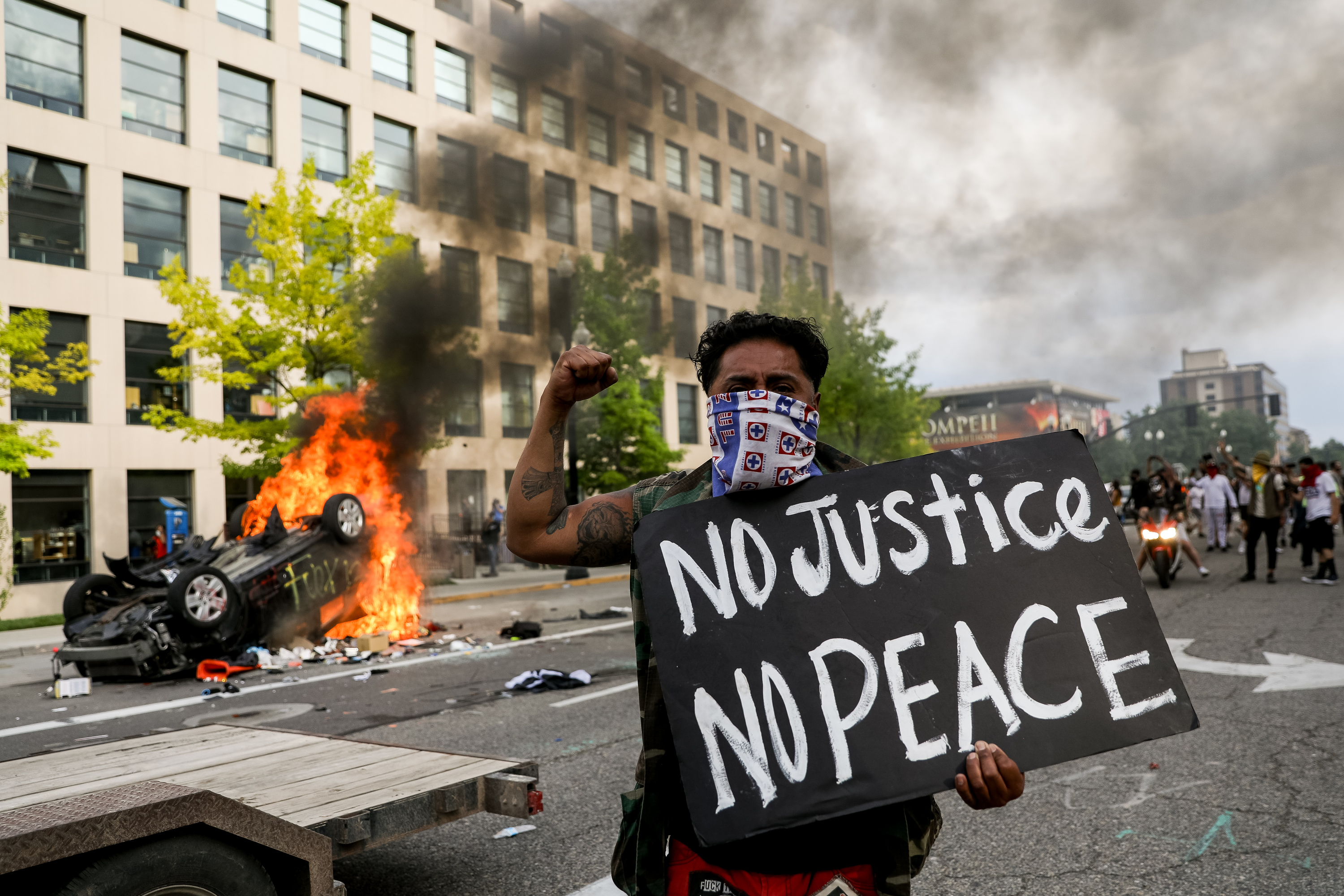 A protester holding a âNo Justice No Peaceâ sign walks past a burning car in downtown Salt Lake City on Saturday, May 30, 2020. Protesters joined others across the nation to decry the death of George Floyd, a Black man, who died while being taken into custody by police in Minneapolis earlier this week.
