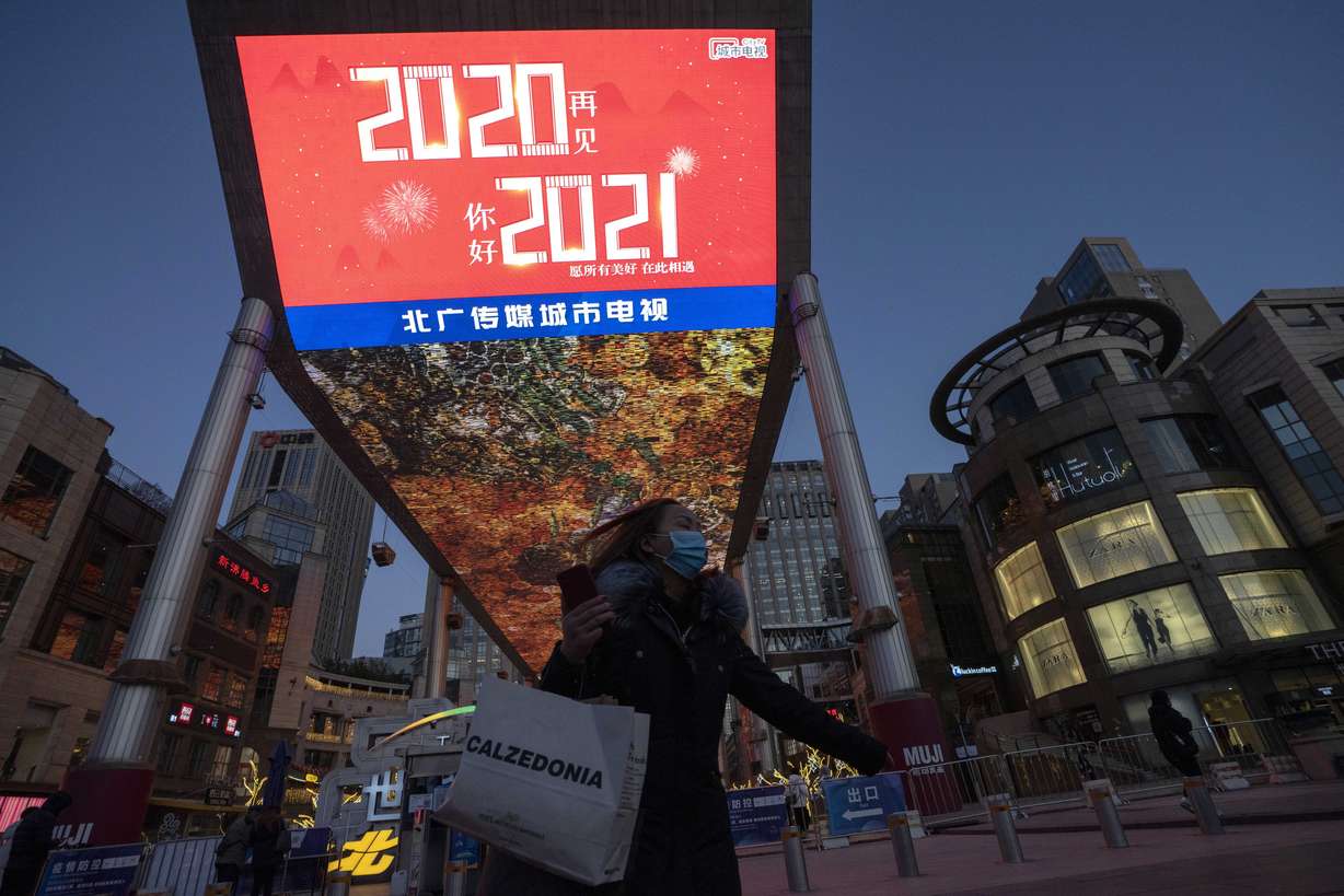 A resident passes by New Year slogans at the entrance to a mall in Beijing Thursday, Dec. 31, 2020. This New Year's Eve is being celebrated like no other, with pandemic restrictions limiting crowds and many people bidding farewell to a year they'd prefer to forget.