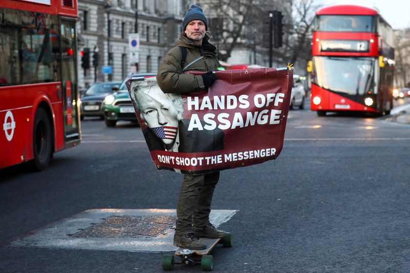 FILE PHOTO: A man rides a skateboard holding a banner with an image of Julian Assange in London, Britain, December 30, 2020. REUTERS/Hannah McKay/File Photo