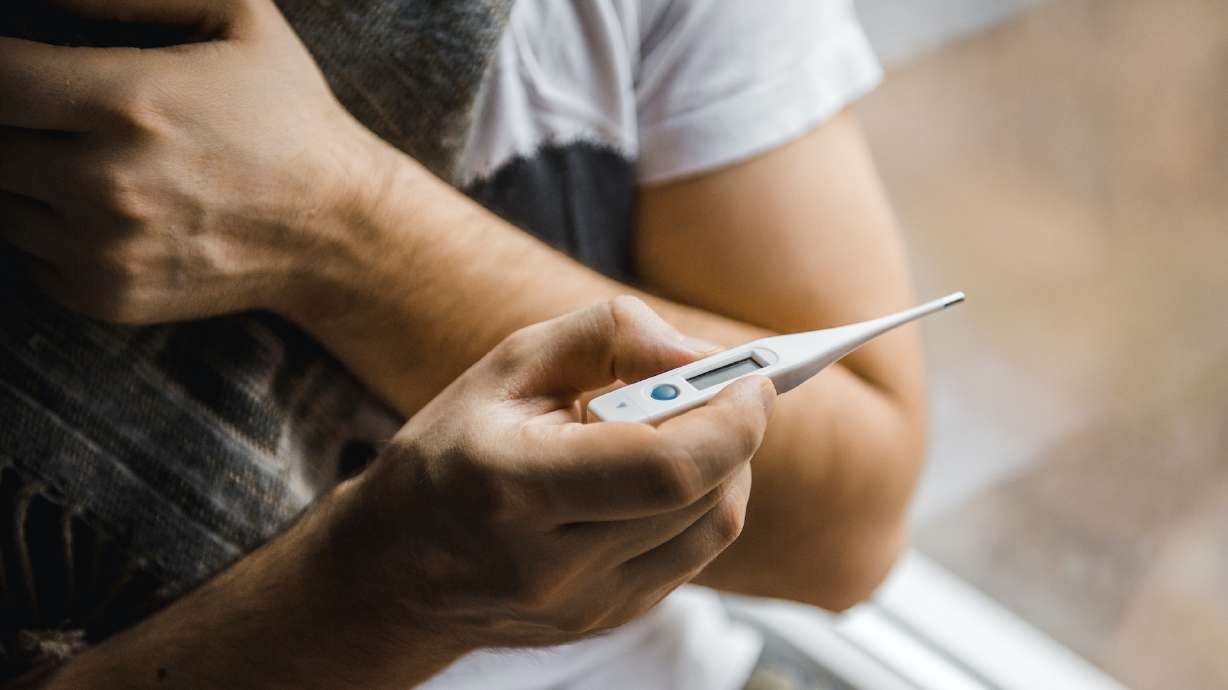 Man feeling bad lying in the bed and looking the thermometer , main focus on the thermometer