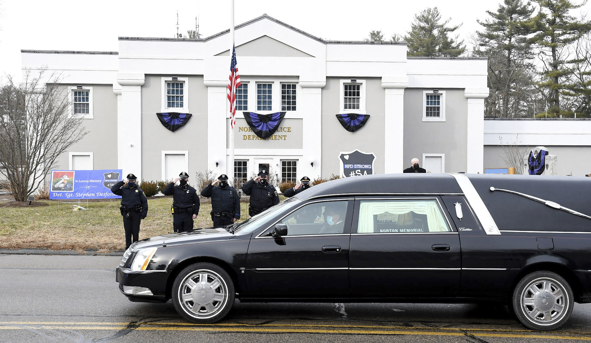 FILE - In this Thursday, Jan. 14, 2021. file photo, Norton, Mass. police salute as a hearse carrying colleague Det. Sgt. Stephen Desfosses briefly stops in front of the police station. Desfosses, 52, a local police officer for 32 years, died of the coronavirus Wednesday in Boston with members of his family by his side, Police Chief Brian Clark said in a statement. Coronavirus deaths are rising in nearly two-thirds of American states as a winter surge pushes the overall toll toward 400,000 amid warnings that a new, highly contagious variant is taking hold. (Mark Stockwell/The Sun Chronicle via AP) [Jan-18-2021]