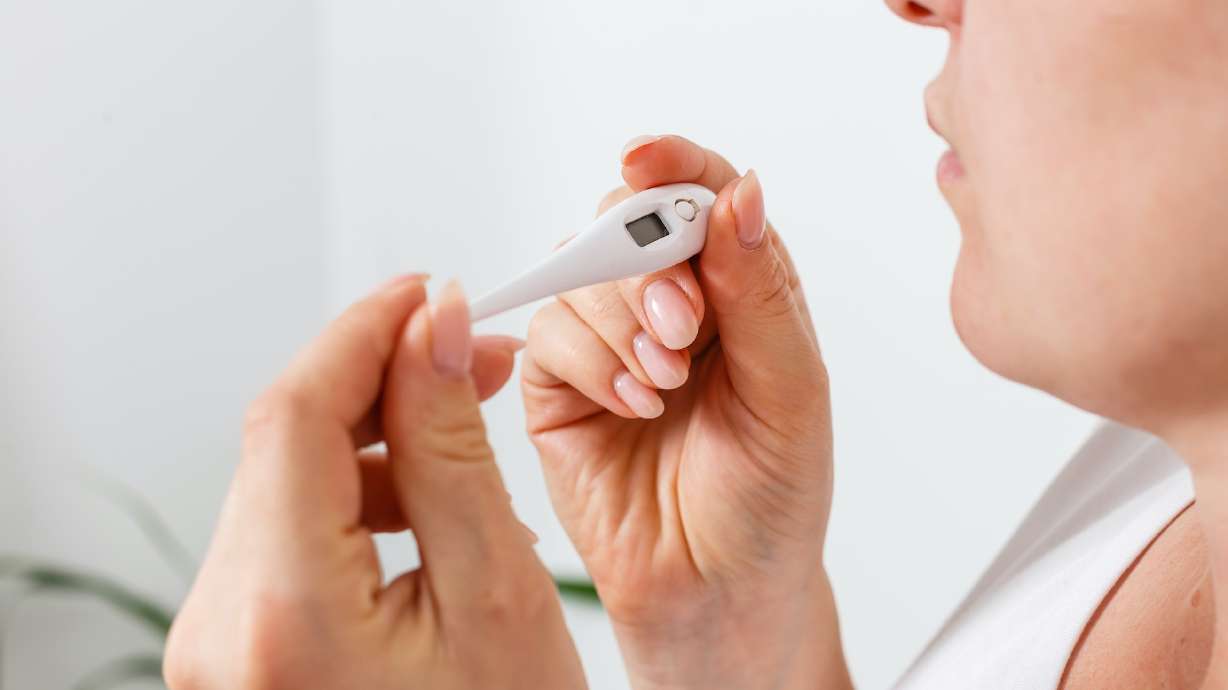 Closeup shot of a woman looking at thermometer. Female hands holding a digital thermometer. Girl measures the temperature. Shallow depth of field with focus on thermometer.