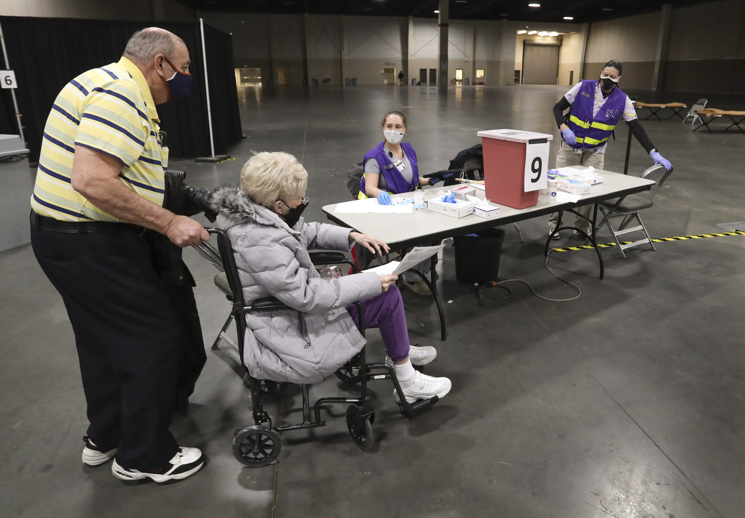 Richard and Joyce Durrant walk to station nine where Megan Boren, center, and Terry Begay, both Salt Lake County Health Department advanced EMTs, are waiting to give them their first dose of the COVID-19 vaccine at the countyâ??s mass vaccination site at the Mountain America Expo Center in Sandy on Monday, Jan. 18, 2021.