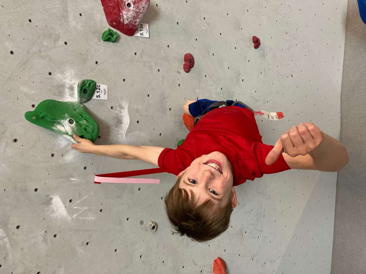 Conner Bailey gives a thumbs up while climbing a 12c grade route at his local climbing gym.