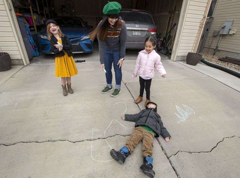 Tess Edwards laughs with Charley Campbell, left, and
Camila Botello, after her son Porter Edwards slides over before
they can finish drawing a chalk outline of him at her home day care
in Eagle Mountain on Friday, Feb. 5, 2021.