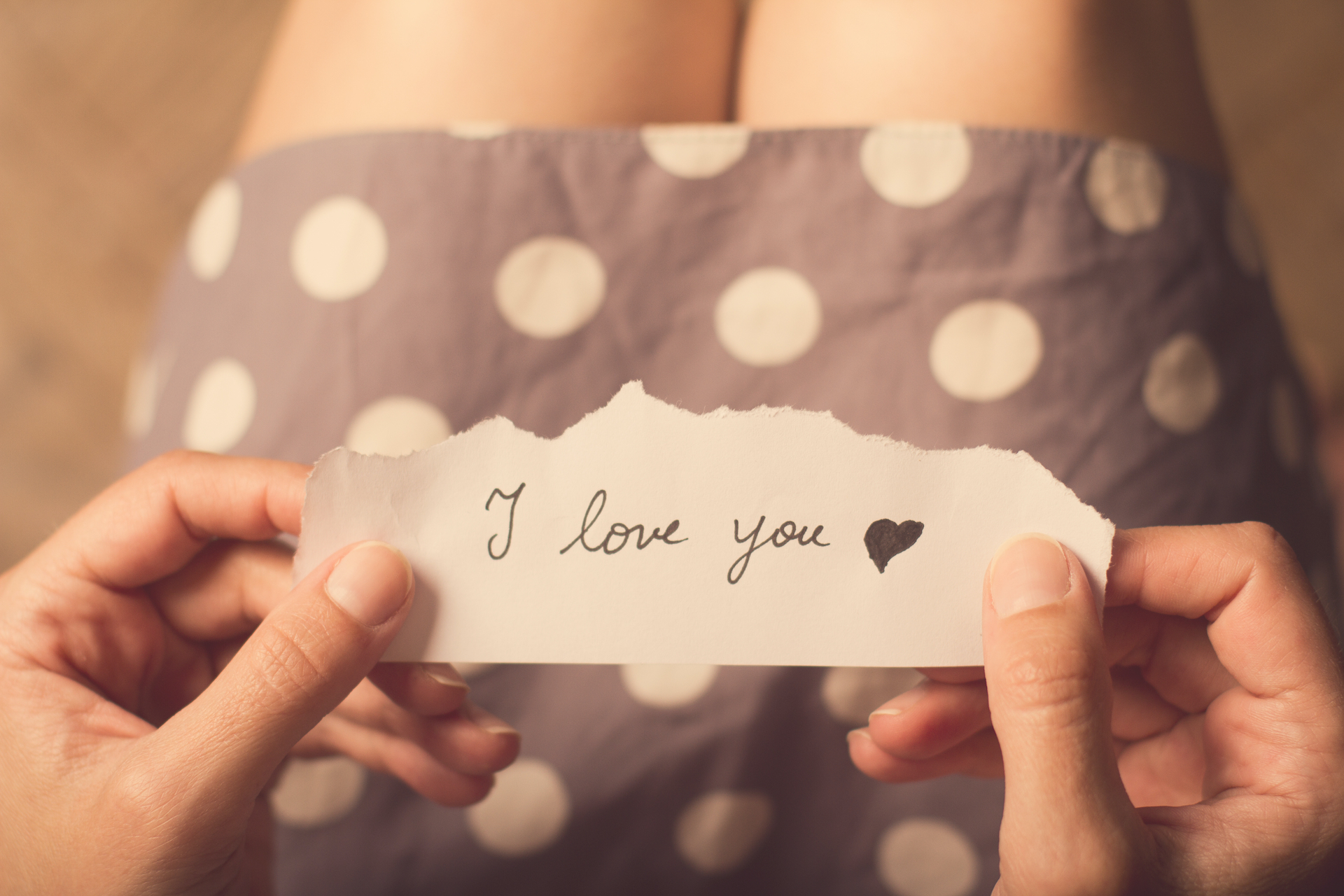 Top view of woman in dotted dress holding a paper message with the text I love you