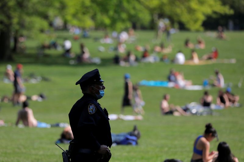 FILE PHOTO: A New York City Police Department (NYPD) officer wearing a protective face mask watches as people gather in the Sheep Meadow in Central Park during the outbreak of the coronavirus disease (COVID-19) in Manhattan, New York City, U.S., May 15, 2020. REUTERS/Andrew Kelly