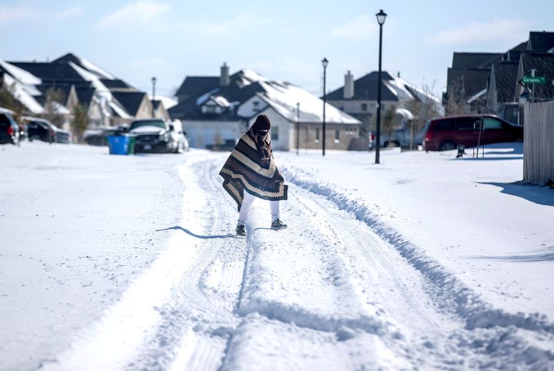 FILE PHOTO: A man walks to his friend's home in a neighborhood without electricity as snow covers the BlackHawk neighborhood in Pflugerville, Texas, U.S. February 15, 2021. Bronte Wittpenn/Austin American-Statesman/USA Today Network via REUTERS/File Photo