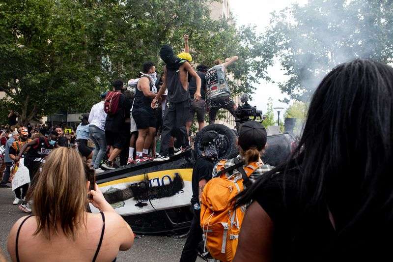 People jump on top of an overturned police car as they protest police brutality in Salt Lake City on Saturday, May 30, 2020. Sen. David Hinkins, R-Orangeville, is sponsoring legislation
that seeks to toughen penalties on rioters while drawing a clearer distinction for when a peaceful protest crosses the line into violent or destructive riot.