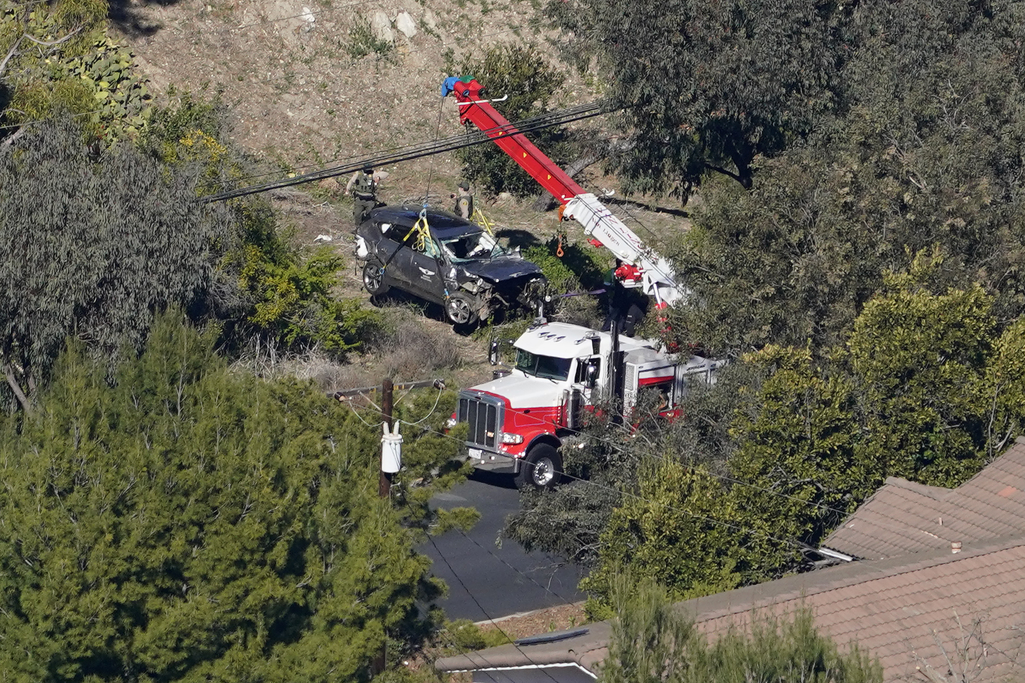 Workers move a vehicle after a rollover accident involving golfer Tiger Woods Tuesday, Feb. 23, 2021, in the Rancho Palos Verdes section of Los Angeles. Woods suffered leg injuries in the one-car accident and was undergoing surgery, authorities and his manager said.