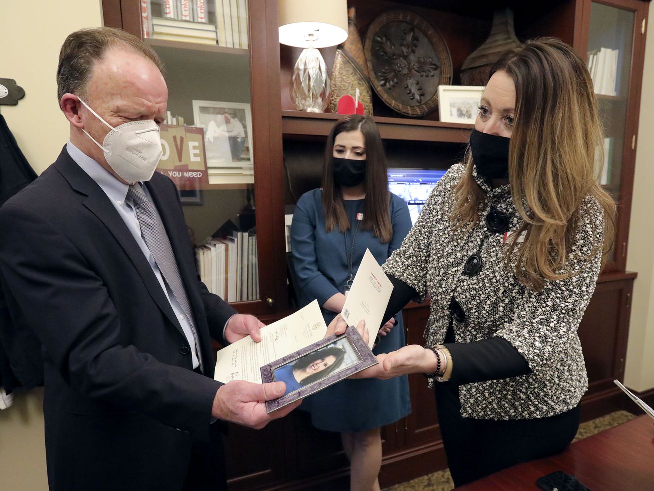 Jim Gamble, left, accepts a framed photo of his late
wife, Allyson Gamble, from Dana Jones, executive director of the
Capitol Preservation Board, right, as Breanna Sibert, deputy
director of the preservation board, looks on at the Capitol in Salt
Lake City on Tuesday, Feb. 16, 2021. Allyson Gamble, who died in
December, was honored by the House for her service as a member of
the preservation board for 19 years, 11 of them as executive
director.