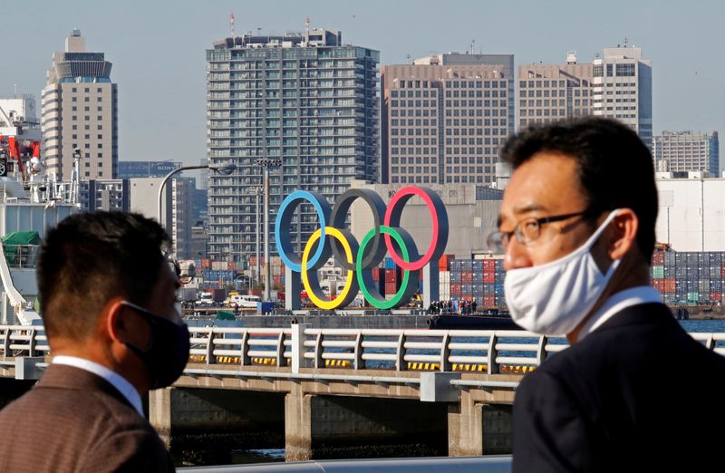 FILE PHOTO: Men wearing face masks watch as giant Olympic rings, which were temporarily taken down in August for maintenance amid the coronavirus disease (COVID-19) outbreak, are transported for reinstallation at the waterfront area at Odaiba Marine Park in Tokyo, Japan December 1, 2020. REUTERS/Kim Kyung-Hoon