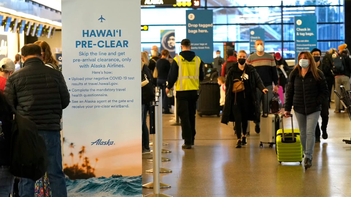 Passengers walk past an Alaska Airlines sign with information on providing COVID-19 test information before flying to Hawaii, Monday, March 1, 2021, at Seattle-Tacoma International Airport in Seattle.