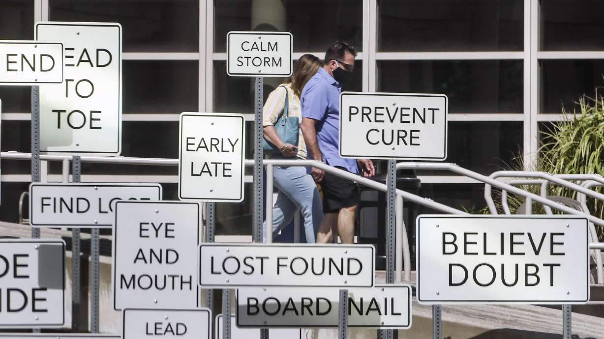 Pedestrians wear masks as they walk past the âPoint of Viewâ art installation in front of the Salt Palace Convention Center in Salt Lake City on Monday, July 27, 2020. The installation, at West Temple and 100 South, was created by Maine artist Aaron T Stephan and features over 150 road signs with diametrical words on them.