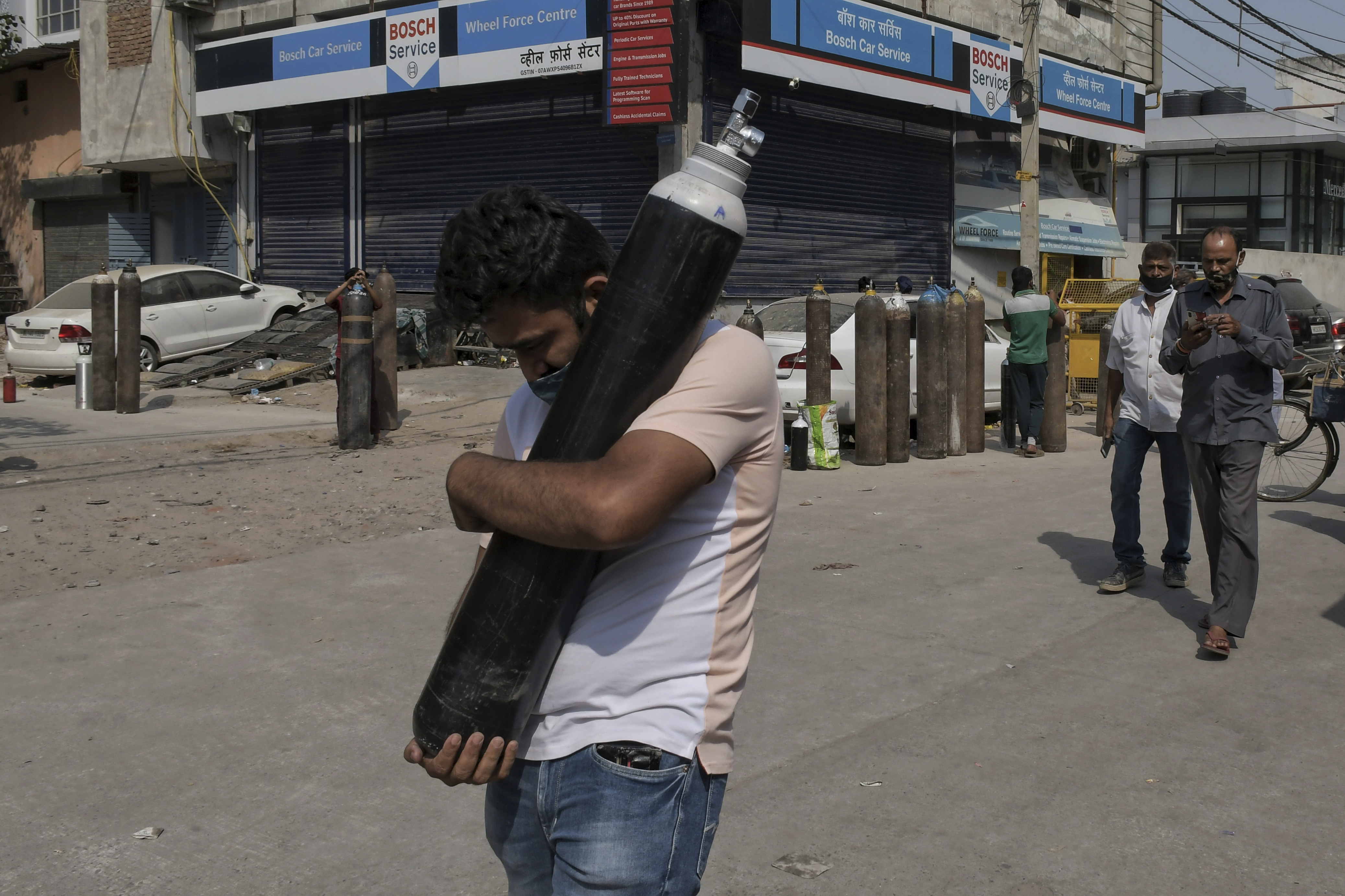 FILE - In this May 3, 2021, file photo, a man walks carrying a refilled cylinder as family members of COVID-19 patients wait in queue to refill their oxygen cylinders at Mayapuri area in New Delhi, India. COVID-19 infections and deaths are mounting with alarming speed in India with no end in sight to the crisis. People are dying because of shortages of bottled oxygen and hospital beds or because they couldn’t get a COVID-19 test. (AP Photo/Ishant Chauhan, File)