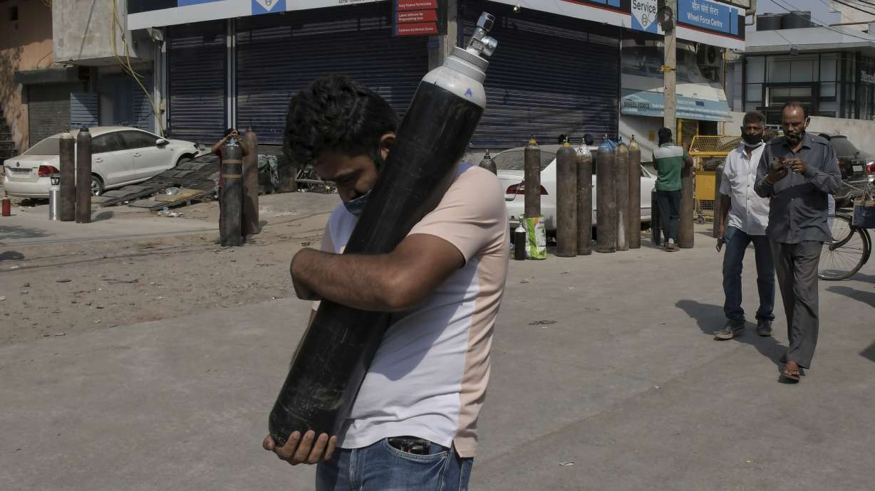 FILE - In this May 3, 2021, file photo, a man walks carrying a refilled cylinder as family members of COVID-19 patients wait in queue to refill their oxygen cylinders at Mayapuri area in New Delhi, India. COVID-19 infections and deaths are mounting with alarming speed in India with no end in sight to the crisis. People are dying because of shortages of bottled oxygen and hospital beds or because they couldn’t get a COVID-19 test. (AP Photo/Ishant Chauhan, File)