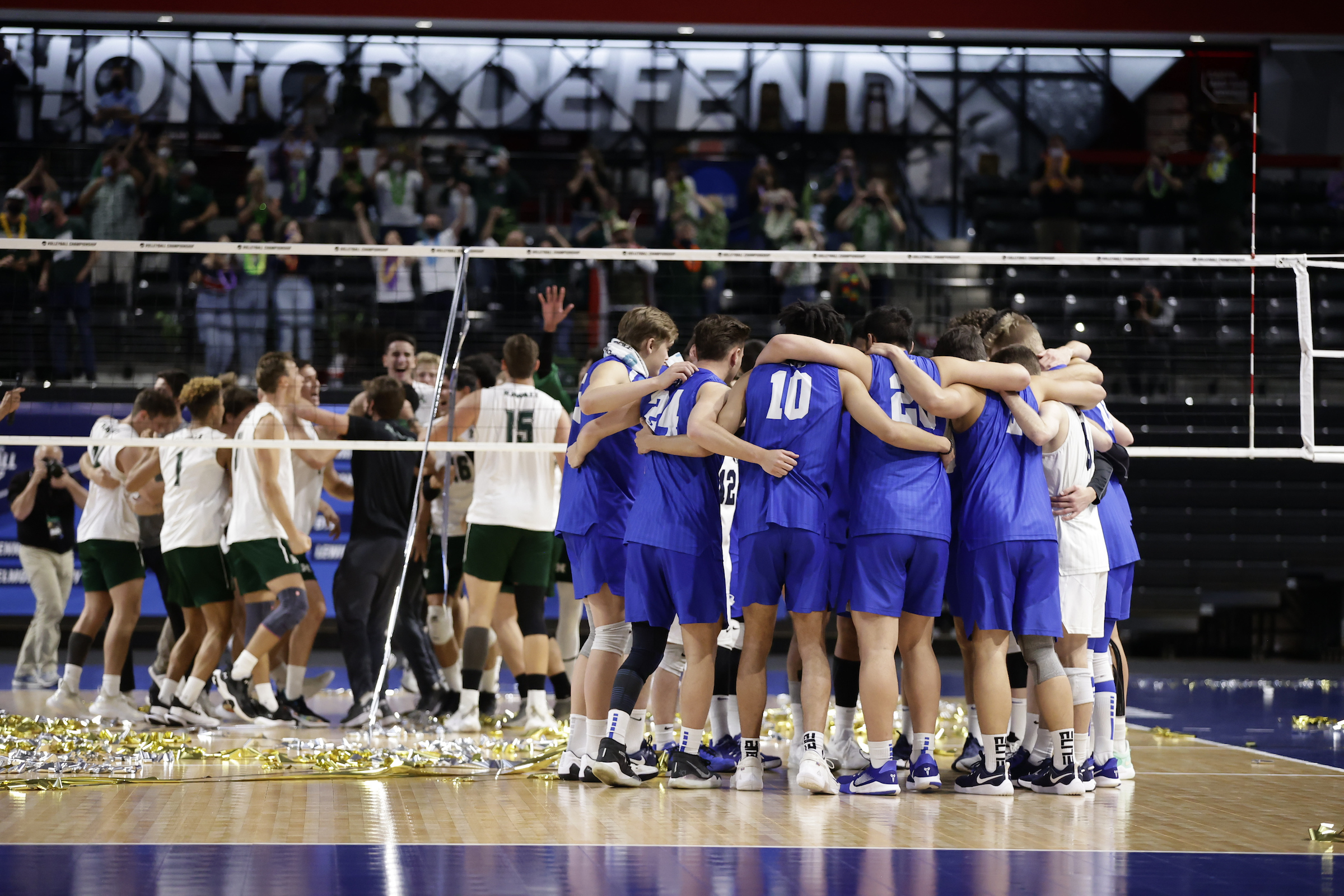 BYU players huddle as Hawaii celebrates on the court following the Rainbow Warriors' 3-0 sweep of the Cougars in the NCAA championship, Saturday, May 8, 2021 in Columbus, Ohio.