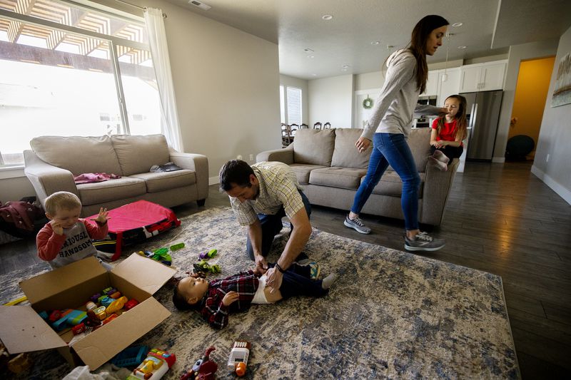 Gavin Mackie, right, plays as his father, James,
center, changes brother Luke’s pants as mom Nachelle and sister
Lily get ready for dinner at their home in Provo on Wednesday,
April 28, 2021.