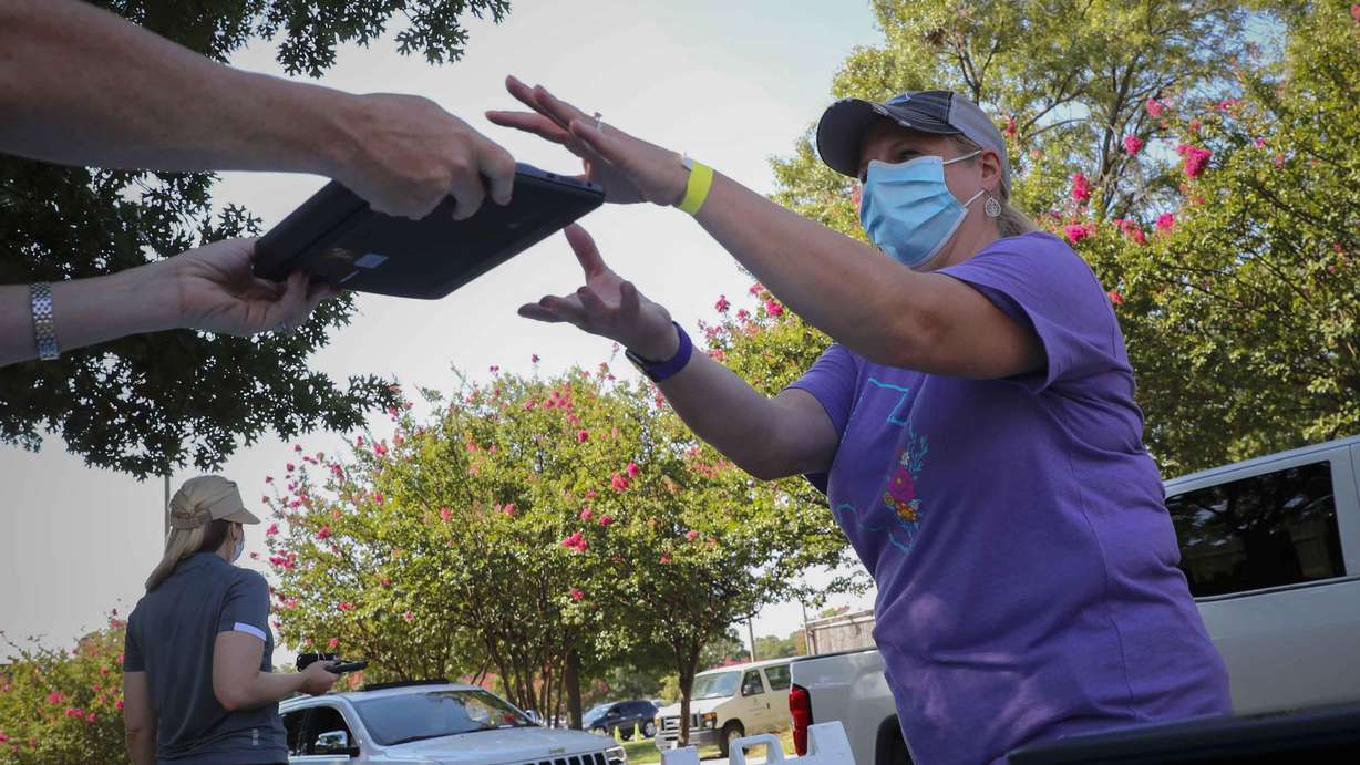 FILE - In this Tuesday Aug. 4, 2020, file photo, volunteer Wendy Dutler hands out computers during a drive-thru giveaway event in Dallas. Americans can begin applying for $50 off their internet bill on Wednesday, May 12, 2021, as part of an emergency government program to keep people connected during the pandemic.