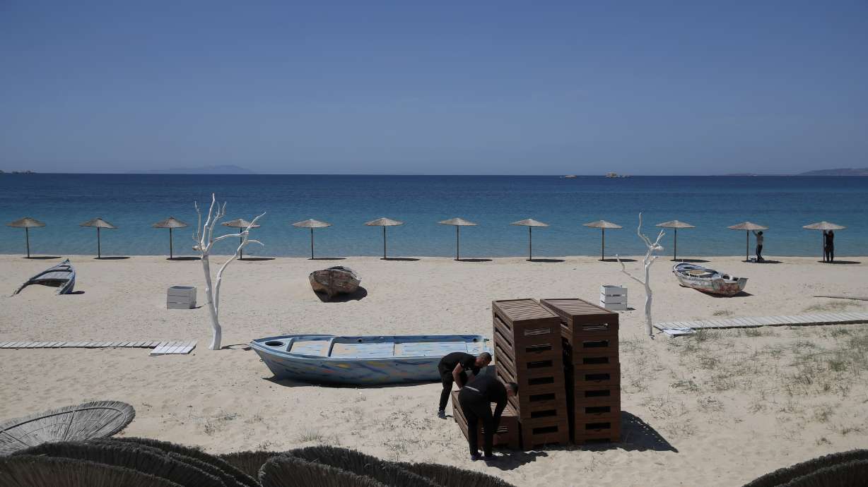 Workers arrange sunbeds as others install umbrellas at Plaka beach on the Aegean island of Naxos, Greece, Wednesday, May 12, 2021. With debts piling up, southern European countries are racing to reopen their tourism services despite delays in rolling out a planned EU-wide travel pass. Greece Friday became the latest country to open up its vacation season as it dismantles lockdown restrictions and focuses its vaccination program on the islands. (AP Photo/Thanassis Stavrakis)