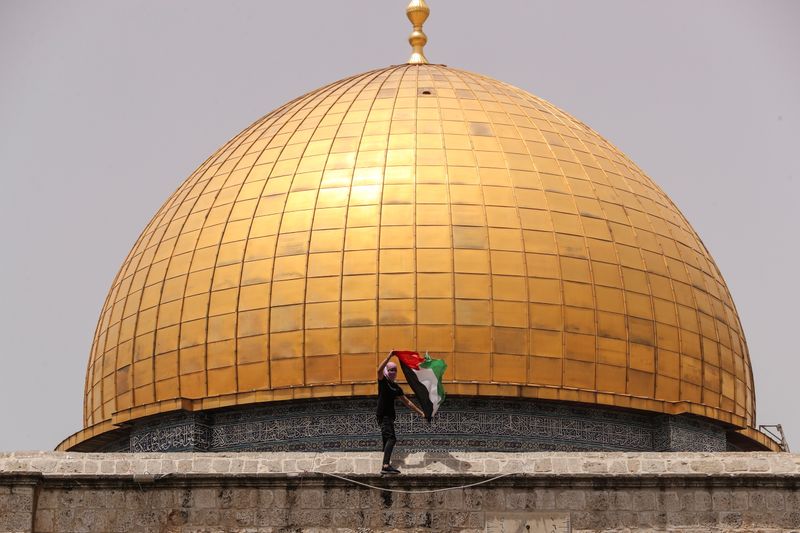 A Palestinian man holds a flag as he stands at the compound that houses Al-Aqsa Mosque, known to Muslims as Noble Sanctuary and to Jews as Temple Mount, in Jerusalem's Old City May 21, 2021.