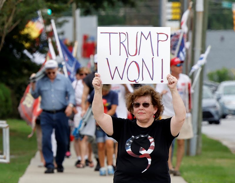 A supporter of former U.S. President Donald Trump wears a QAnon shirt while holding a sign stating he won the 2020 election, outside the North Carolina GOP convention in Greenville, North Carolina, on June 5, 2021.