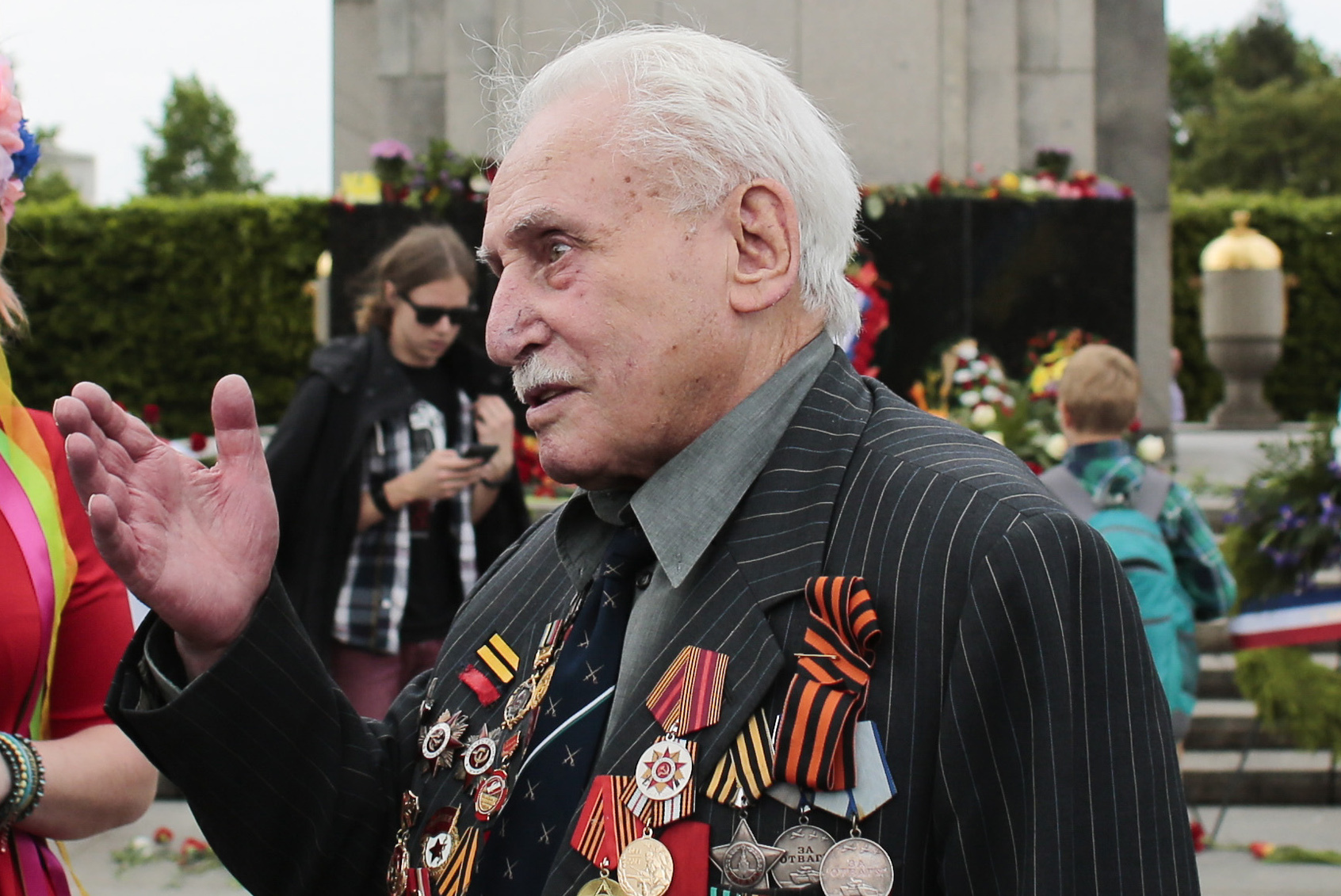 FILE  - In this Friday, May 8, 2015 file photo, Soviet war veteran David Dushman, 92, center, speaks to people holding Ukrainian flags as he attends a wreath laying ceremony at the Russian War Memorial in the Tiergarten district of Berlin, Germany. Dushman, the last surviving Allied soldier involved in the liberation of Auschwitz, has died. The Jewish Community of Munich and Upper Bavaria said Sunday, June 6, 2021 that Dushman had died a day earlier in a Munich hospital at the age of 98. As young Red Army soldier, Dushman flattened the forbidding fence around the notorious Nazi death camp with his tank on Jan. 27, 1945. (AP Photo/Markus Schreiber, File)