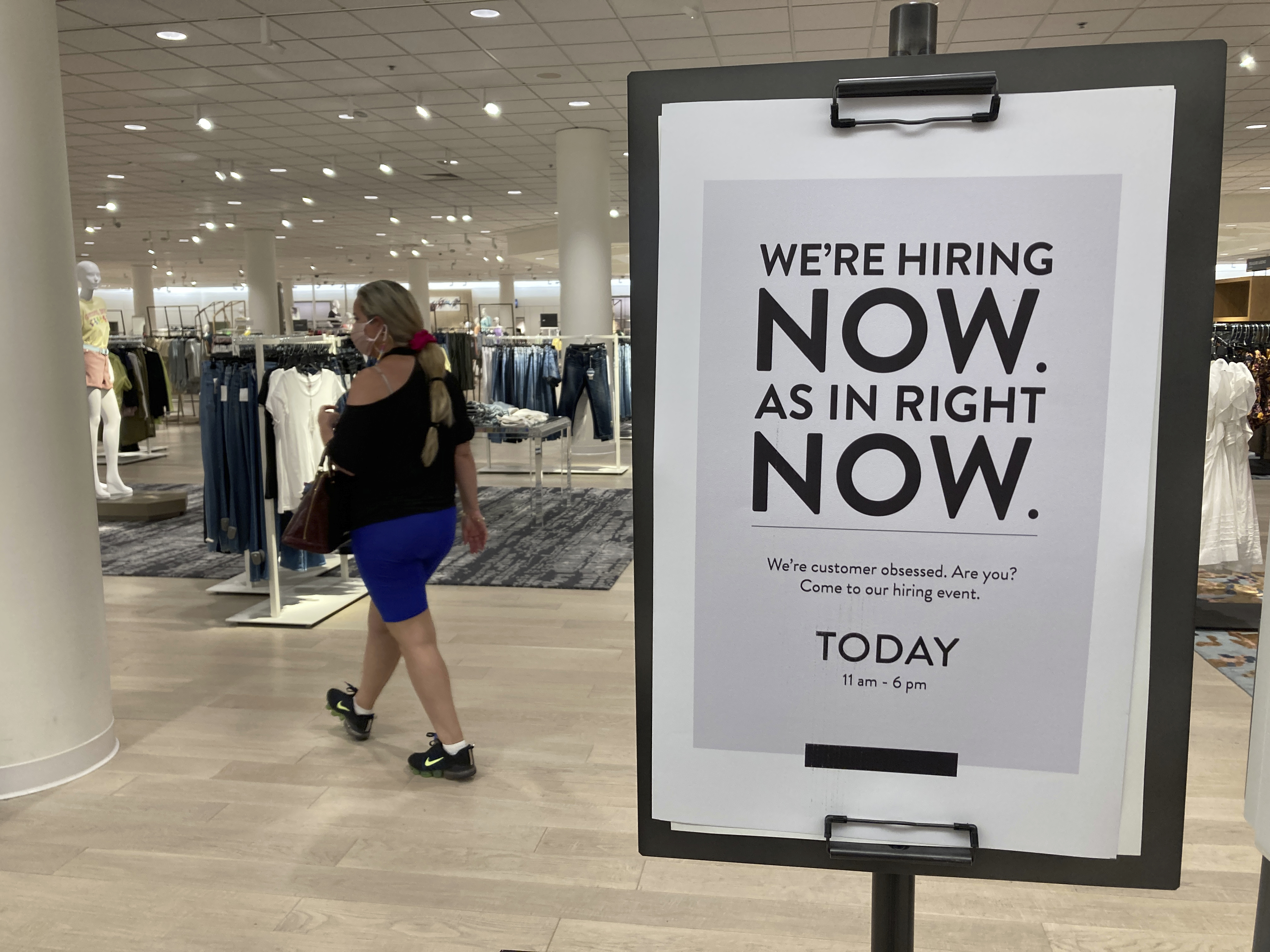 A customer walks behind a sign at a Nordstrom store seeking employees, Friday, May 21, 2021, in Coral Gables, Fla. The number of Americans seeking unemployment benefits dropped last week to 406,000, a new pandemic low and more evidence that the job market is strengthening as the virus wanes and economy further reopens.
