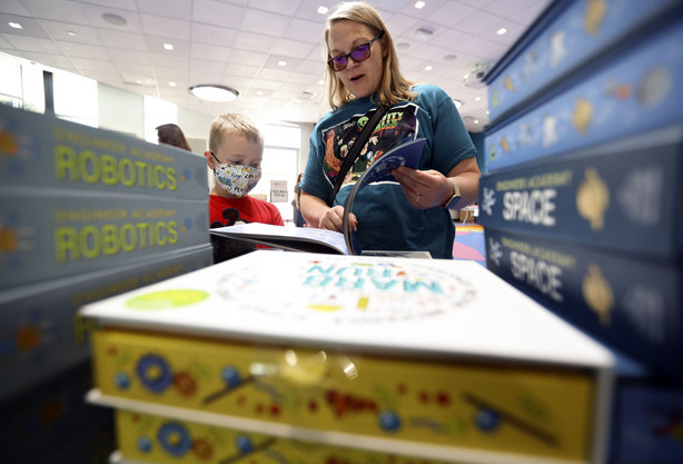 Toby Berry picks out a book with the help of his mother, Charisse Berry, at the Salt Lake County Library in Kearns on Thursday, June 10, 2021. One thousand children will receive shoes, books and a meal through a partnership with the Salt Lake County Library, Operation Warm, MolinaCares, The Sorenson Legacy Foundation and the Utah Food Bank.
